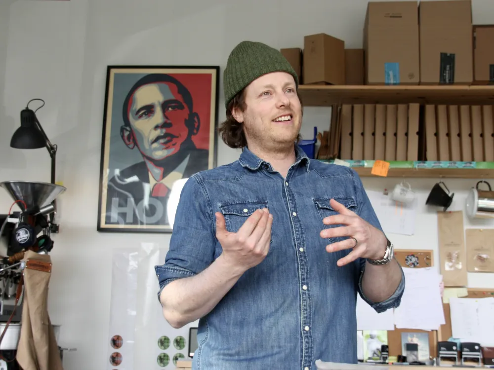 En mann på en kafé som forklarer om kaffe. Et bilde i bakgrunnen.