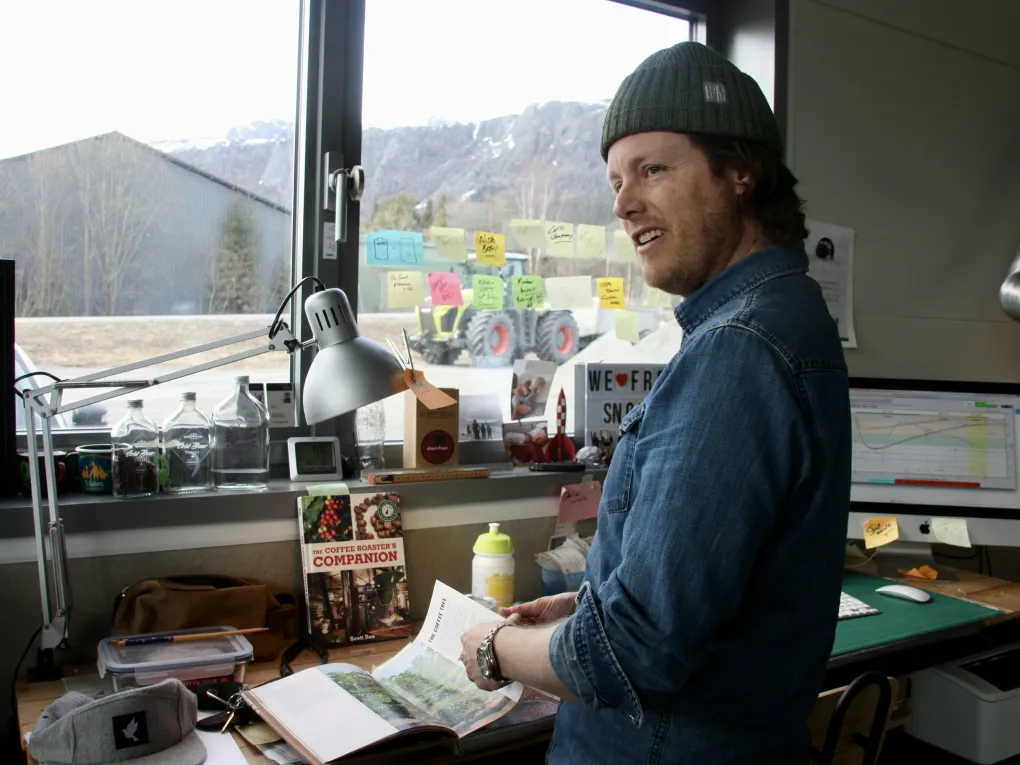 A man wearing a green hat, flipping through a book. A tractor and a building in the background.