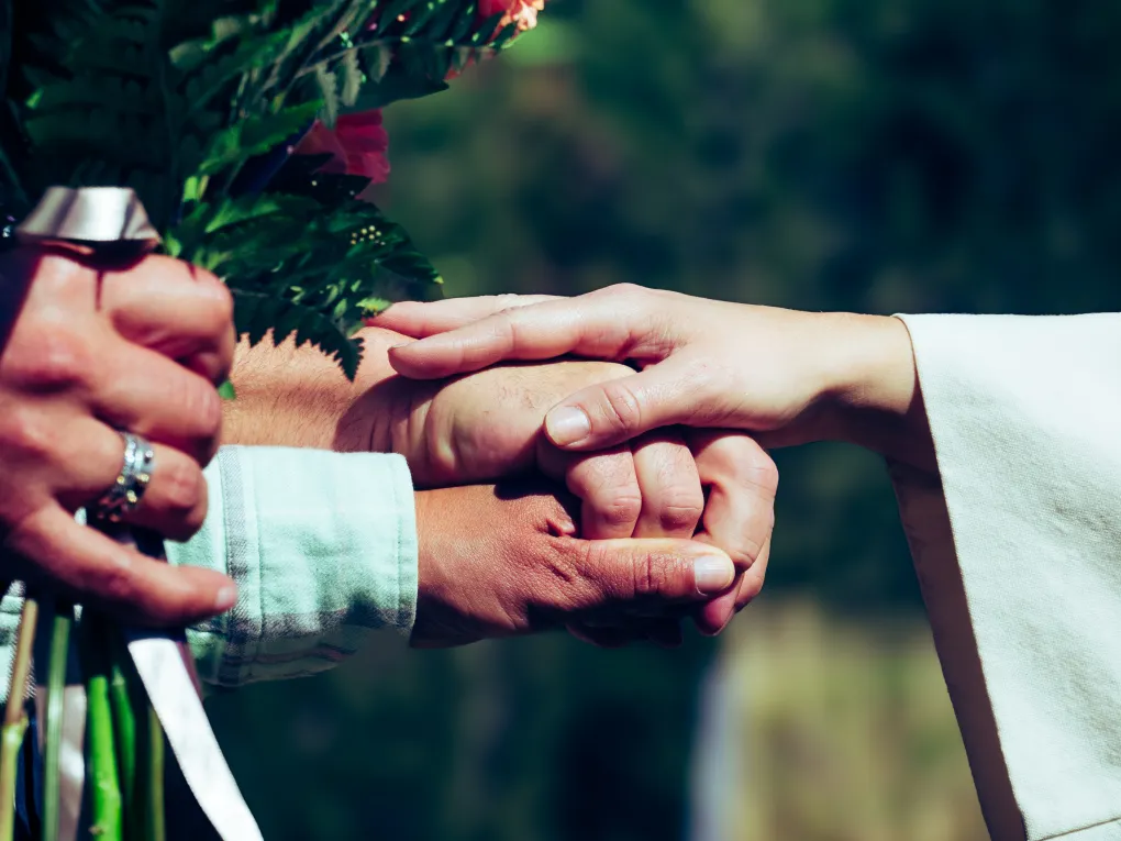 Nærbilde av to hender som holder hverandre, med en hånd på topp. Blomstebukett