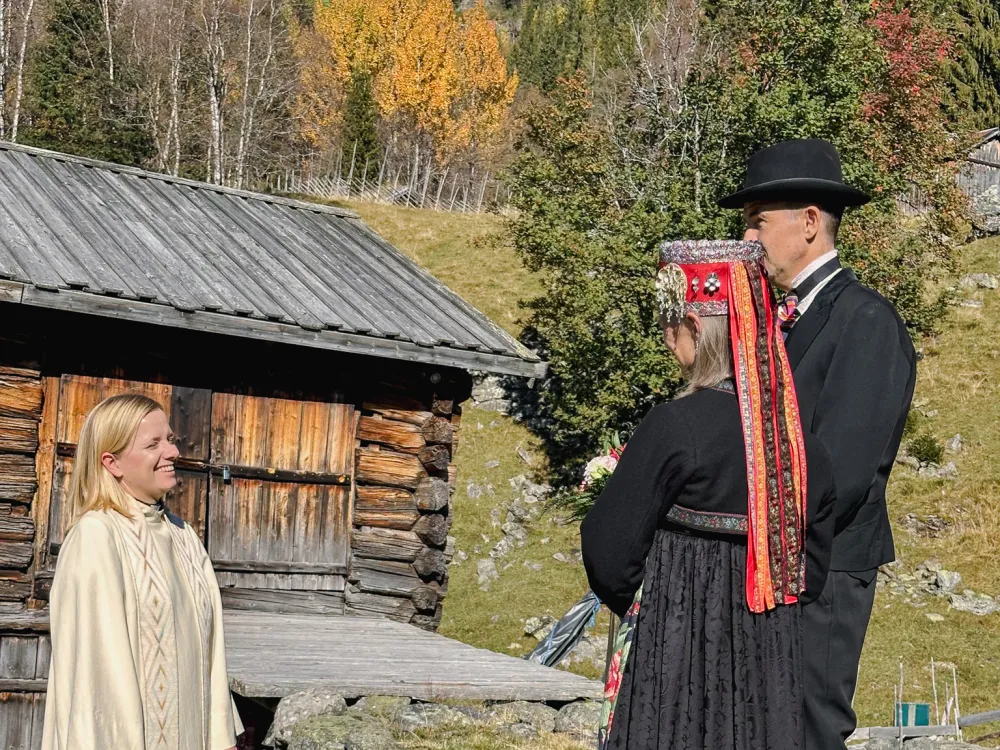 Mennesker på gårdstun. Natur og gammel bygning i bakgrunn