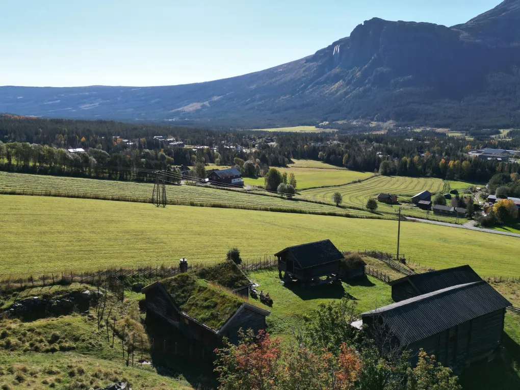 Bygninger på tun. Fjellside, foss og natur i bakgrunn