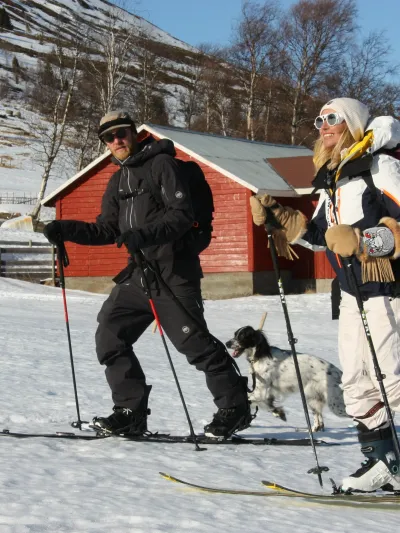To mennesker og en hund som går på ski sammen. Hunden løper etter