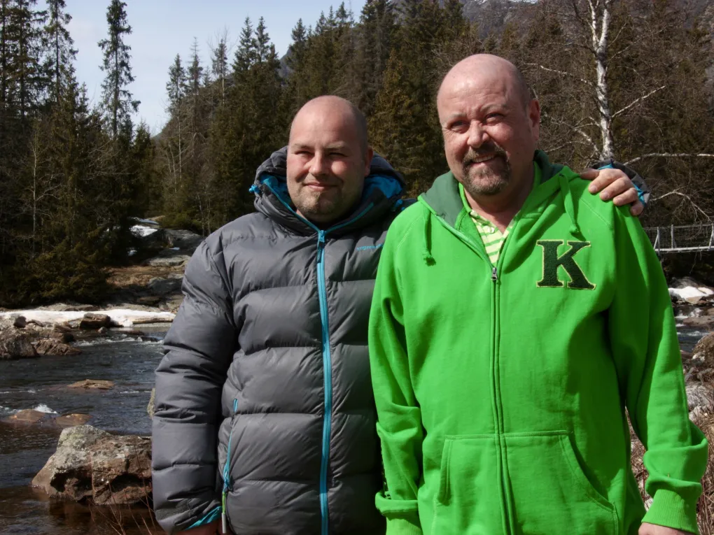 To menn som holder rundt hverandre og smiler