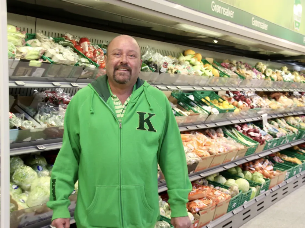 Mann/Oddbjørn smiler til kameraet. Står foran grønsakene