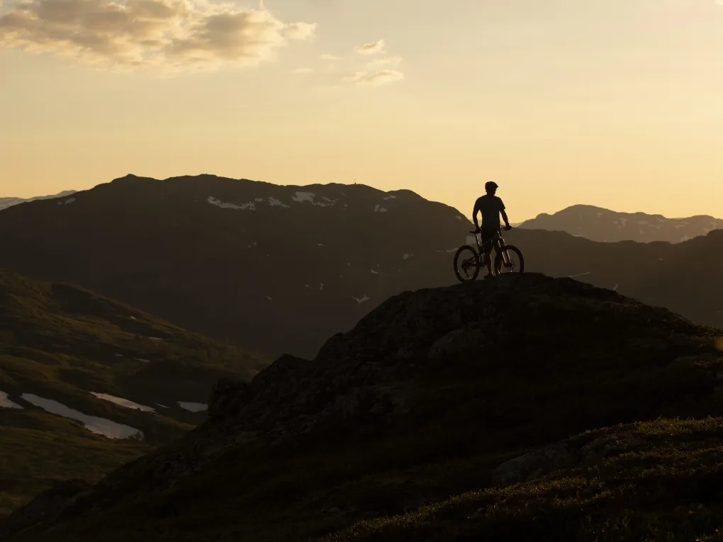 Mann på sykkel på toppen av et berg. Solnedgang