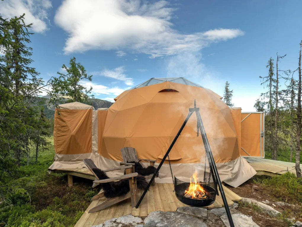 Bilde av ett stort telt med bål og to stoler i front