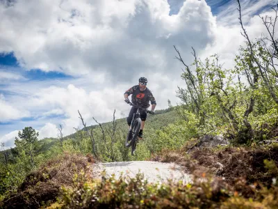Mann som hopper med sykkel på sti i fjellet.