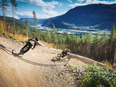 Den Ravinde i Nesbyen Foto Lars Storheim, to personer som sykler og i bakgrunnen er det fjell og skog.