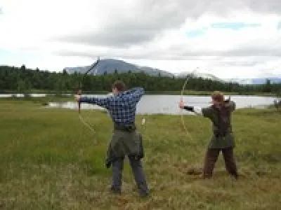 To som skyter med pil og bue ute i naturen/fjellet.