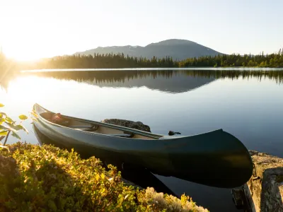 Grønn kano, i bakgrunnen er det skog, fjell og solnedgang.