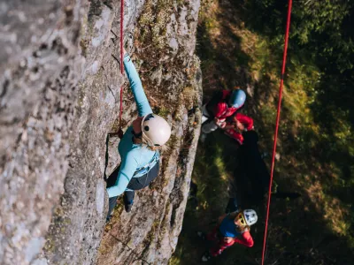En dame som klatrer oppover med to stk som står under og titter