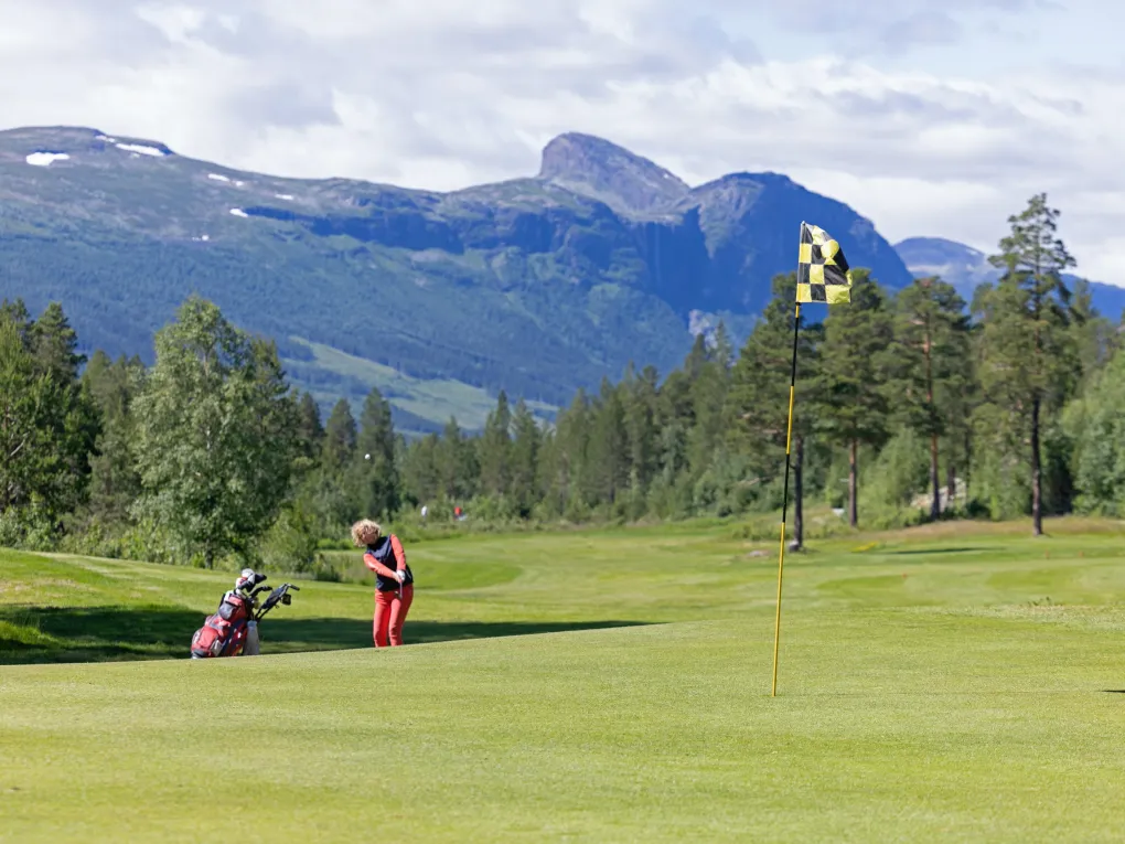 Anstandsbilde av dame ikledd oransj, som slår noen baller på golf coursen i solen.