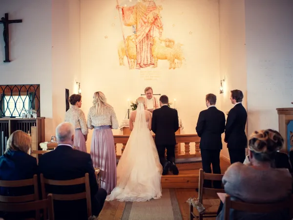 Bilde av to mennesker som står ved alteret og blir viet med publikum rundt