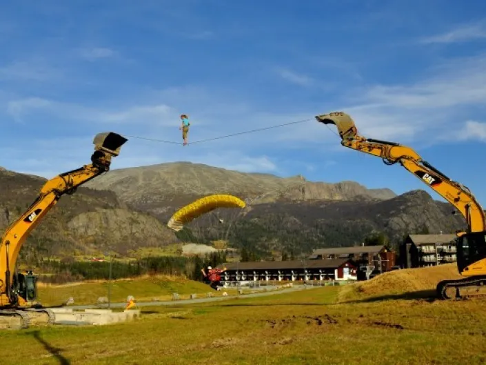 Mennesker som går slakk line mellom to gravemaskiner