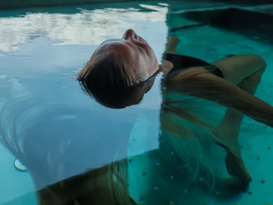 Jente som ligger med hodet opp i poolen.