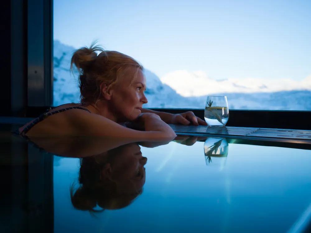 Dame som sitter i mini bassenget på skarsnuten og ser utover utsikten av de snødekkede fjellene.