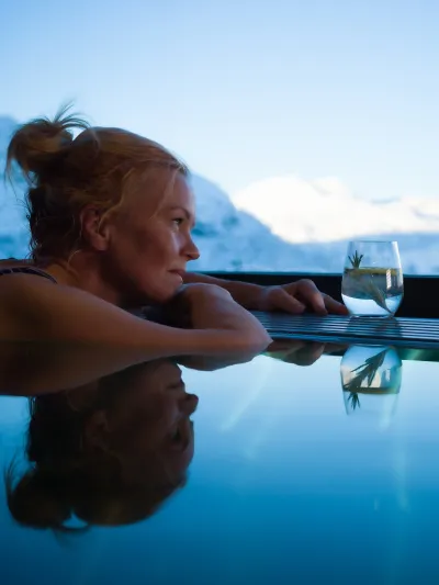 Dame som sitter i mini bassenget på skarsnuten og ser utover utsikten av de snødekkede fjellene.