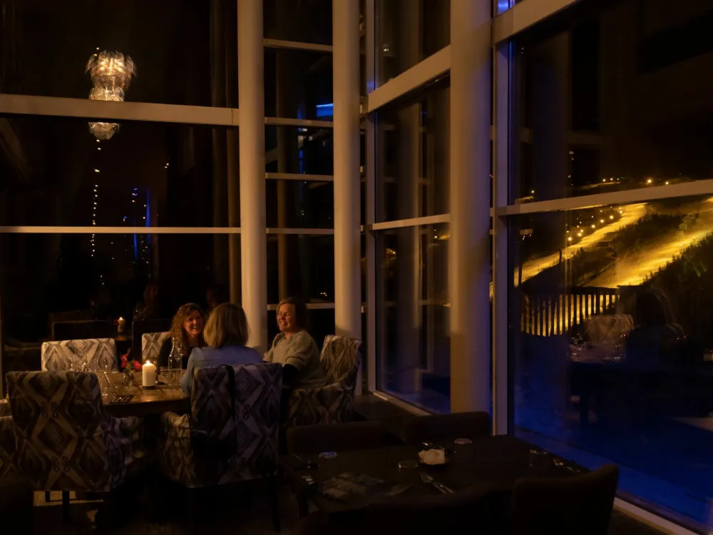 Tre damer som hygger seg på skarsnuten, i bakgrunnen er det skibakken på kveldstid.