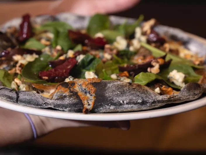 To hender som holder en svart pizza med delikat topping.