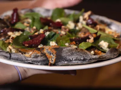 To hender som holder en svart pizza med delikat topping.