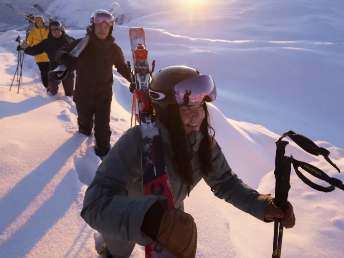 Gjeng som går på topptur i solnedgang, med skiene på skuldrene.