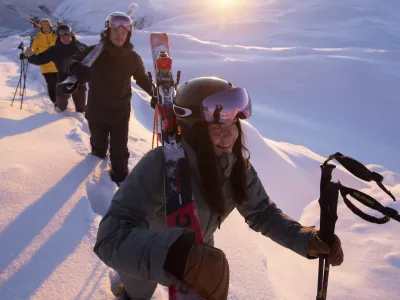 Gjeng som går på topptur i solnedgang, med skiene på skuldrene.