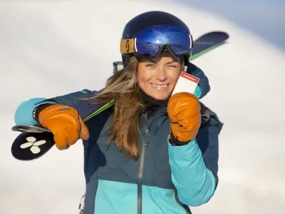 Dame med ski-kort i hånden og skiene på skulderen.