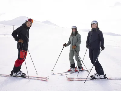 To damer og en mann som står i skibakken og ser inn i kameraet, ikledd skiklær.