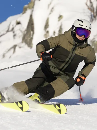 Dame ikledd grønt som kjører ski nedover bakken.