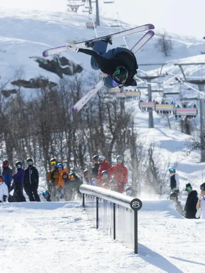 Gutt som gjør et triks i en rail i parken, og i bakgrunnen står publikum og heier.