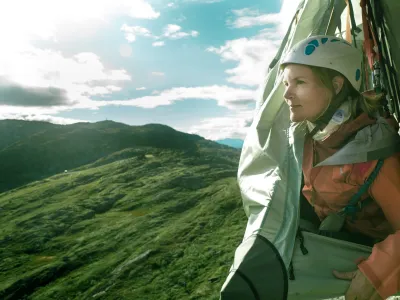 Dame som titter ut av skysleeping teltet, med fjellene i bakgrunnen.