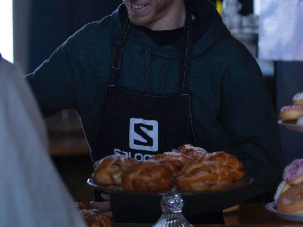 Mann som står i skranken på en kafe og selger kanelboller i solheisen