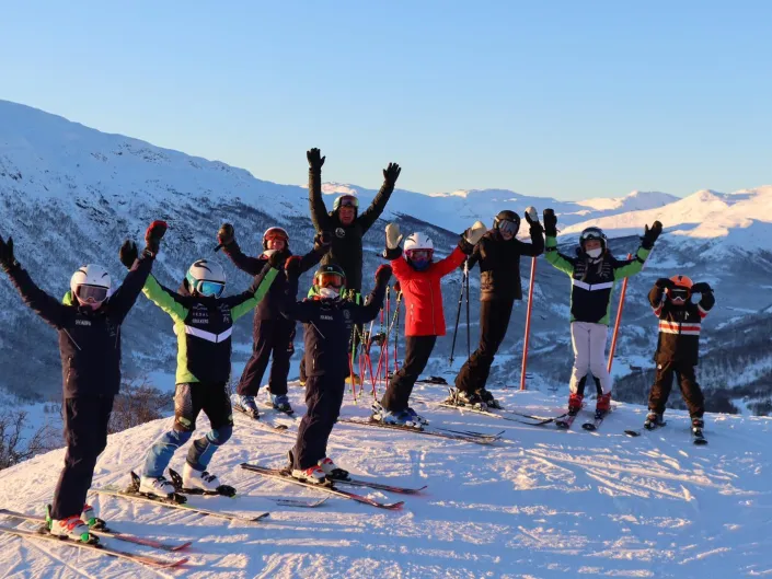 Gruppe mennesker som holder armene er været og står på slalom i solheisen Hemsedal