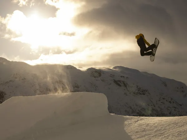 Mann som hopper med snowboard i solheisen