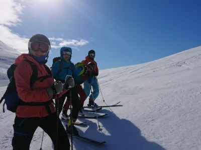 Topptur i fjellet om vinteren, gjengen kjører ned på randone i sola.