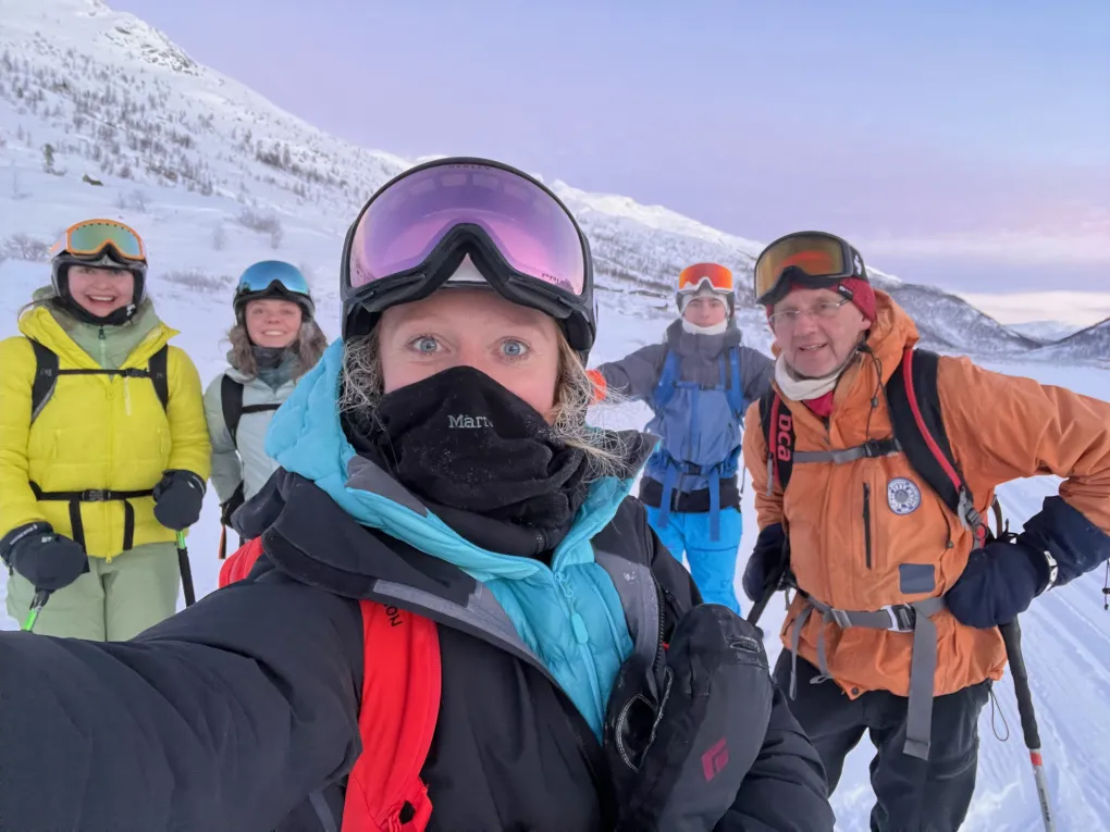 En gjeng på tur i fjellet om vinteren, bak dem er det lilla himmel.