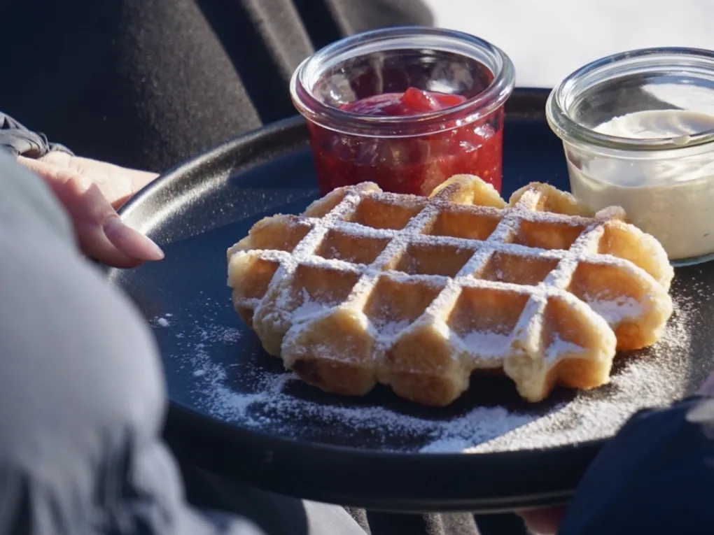 Person som sitter ned med en tallerken med belgisk vaffel, syltetøy og rømme