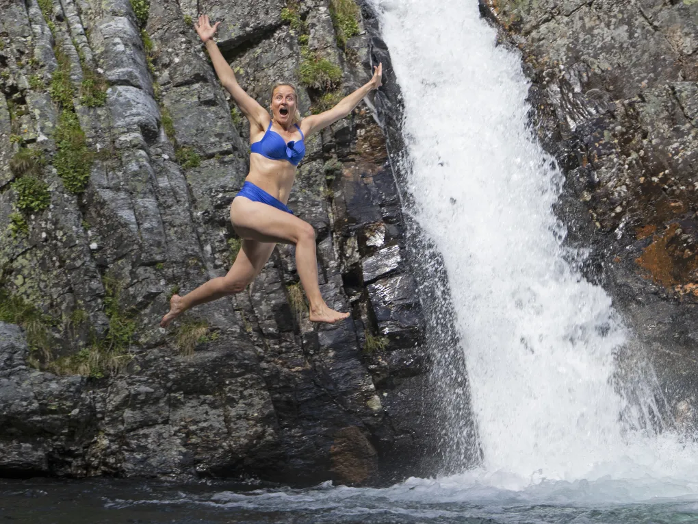 Dame som hopper med armene ut, fossefall.