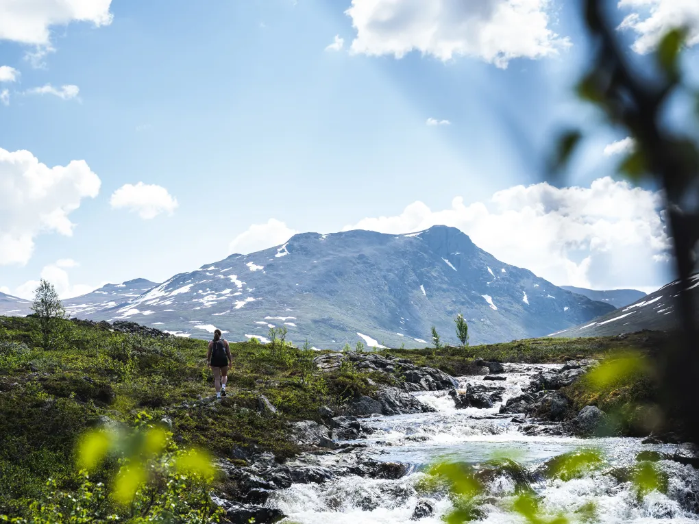 En dame som går ved siden av en elv, oppover i fjellet.