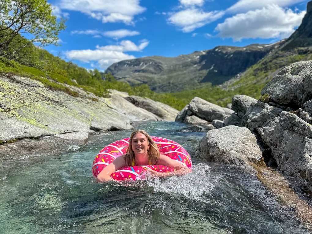 Dame som bader i donut i elva (sommer) og ser mot kameraet.