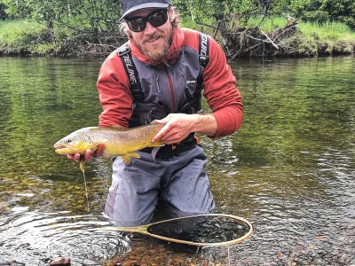 Mann som holder en fisk mens han står på kne i vannet