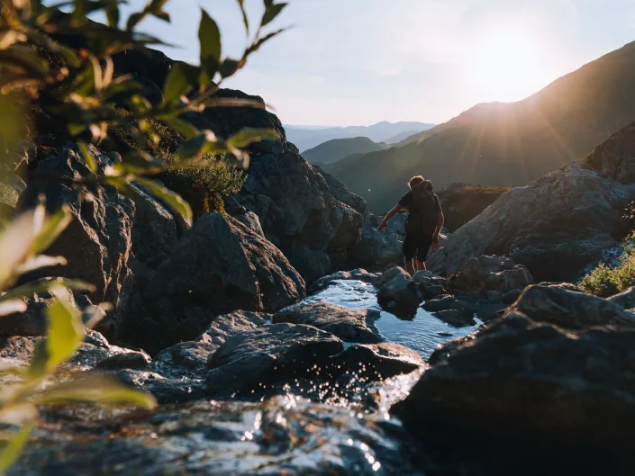 Mann som går i fjellet med solnedgang i bakgrunnen, samt en liten bekk.