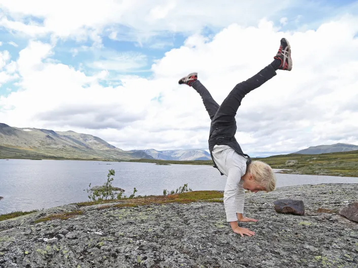 Liten gutt som står på henda i fjellet.