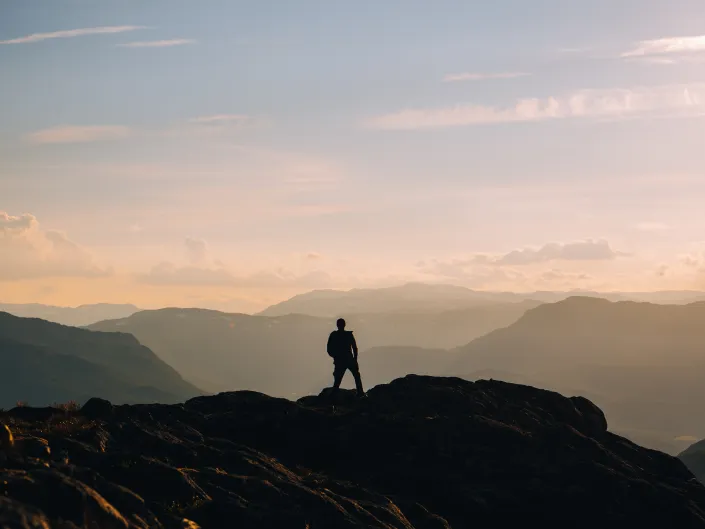 Person på toppen av et fjell i morgen disen.
