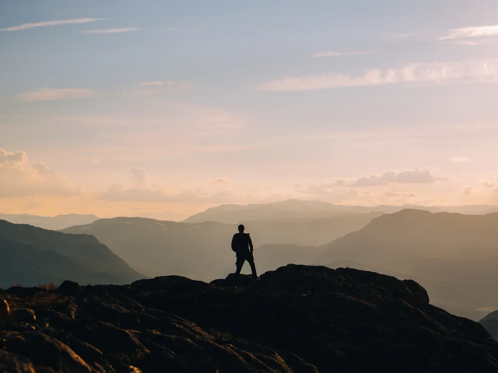 Person på toppen av et fjell i morgen disen.