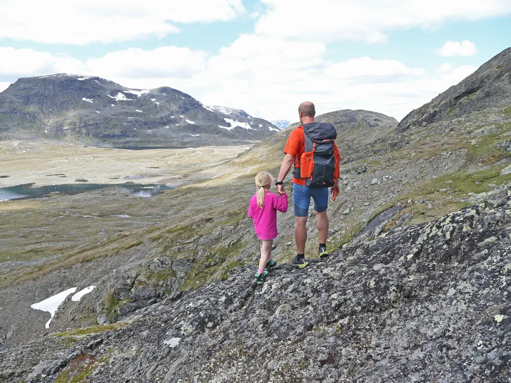 Mann og liten jente, holder hender i fjellet.
