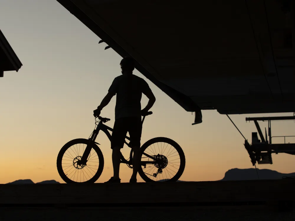 Mann og sykkel som står på toppen av heisen i Hemsedal under solnedgangen