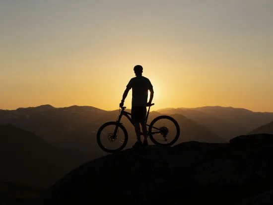 Mann og sykkel som står på toppen av et fjell i solnedgangen