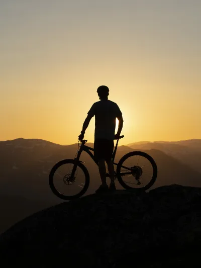 Mann og sykkel som står på toppen av et fjell i solnedgangen