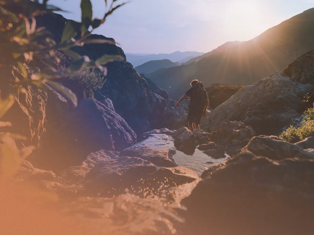 Mann som går tur i fjellet med stein og sol i bakgrunnen.